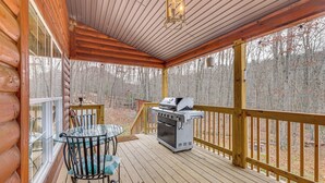 Eine Holzterrasse mit Grill und einem Glastisch mit Stühlen.