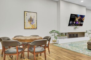 Een vergaderruimte met een ronde tafel en zes stoelen, een groot abstract schilderij, een flatscreen-tv waarop filmposters worden getoond, en een receptiebalie met een plant.