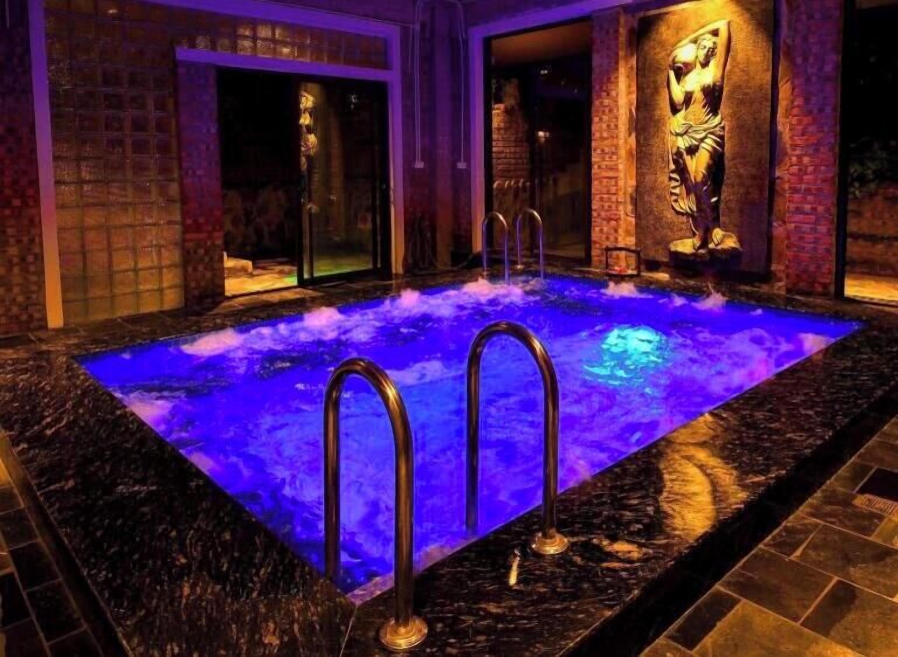 A heated outdoor swimming pool with two metal ladders, surrounded by stone walls and a statue.