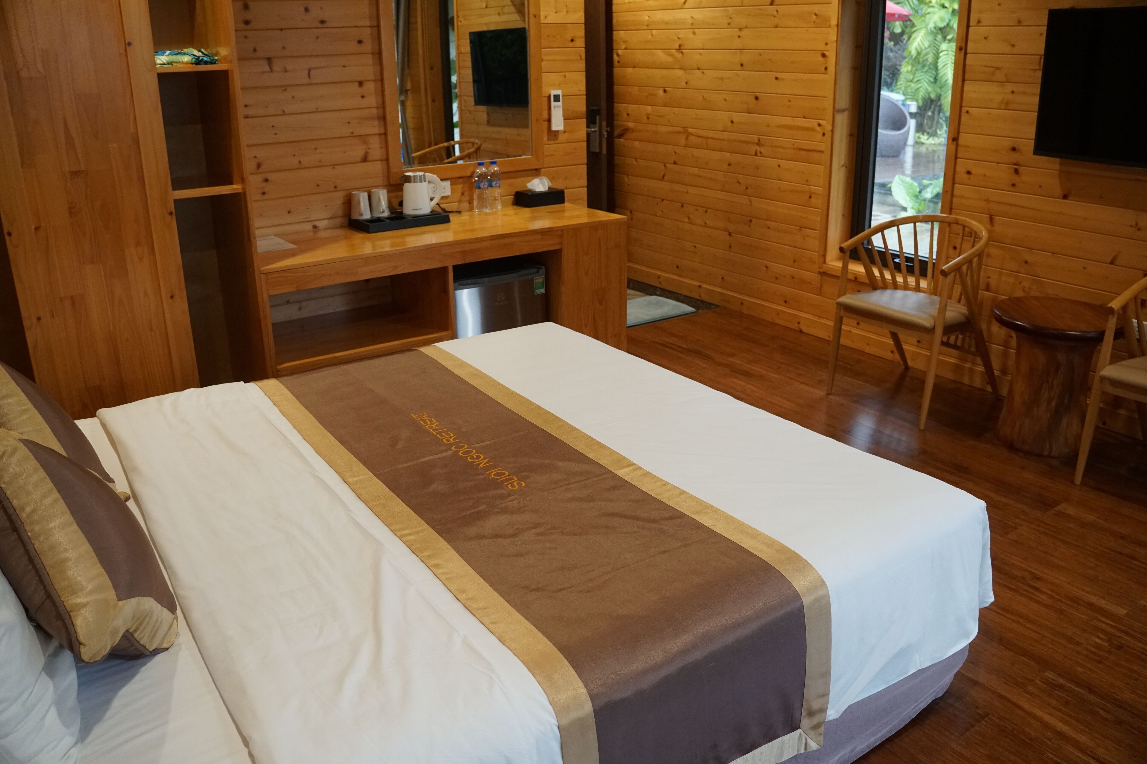 Quarto estilo cabana de madeira, com uma cama, uma escrivaninha, uma cadeira e uma televisão.