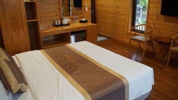 Quarto estilo cabana de madeira, com uma cama, uma escrivaninha, uma cadeira e uma televisão.