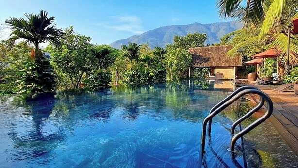 Una piscina cristallina circondata da vegetazione lussureggiante e con le montagne sullo sfondo.
