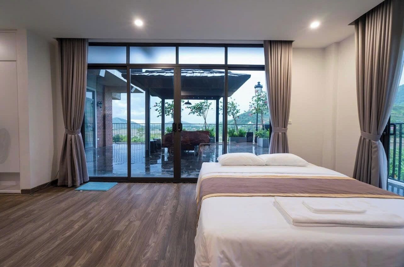 A bedroom with a large bed, a sliding glass door leading to an outdoor area with a covered seating space.