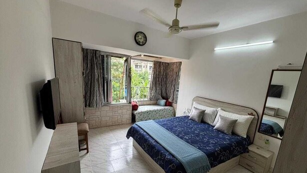 Ein Schlafzimmer mit einem Bett, einem Schreibtisch, einem Stuhl, einem Fenster mit Vorhängen, einem Deckenventilator und einer Uhr.