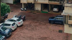 Ein mehrstöckiges Wohnhaus mit Balkonen, ein Parkplatz mit mehreren Autos und eine Palme im Vordergrund.