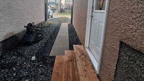 A narrow outdoor area with a gravel path, a wooden bench, and a small black object on the ground.