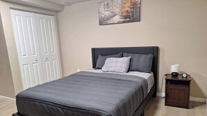 A bedroom with a bed, a nightstand, a clock, and a door.
