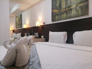 A hotel room with a large bed, two wall-mounted lamps, a painting, and a nightstand with a kettle and a cup. - AtWhitePatong (Patong)