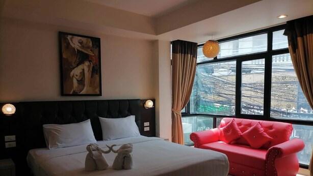 A hotel room with a large bed, a red sofa, a painting on the wall, and a view of the city through the window. - AtWhitePatong (Patong)