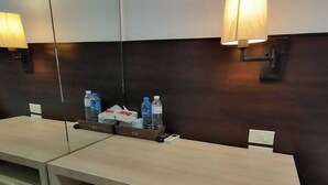 A hotel room with two wooden desks, each with a mirror and a wall-mounted lamp. There are two water bottles on the desks, and a small trash bin is visible. - AtWhitePatong (Patong)