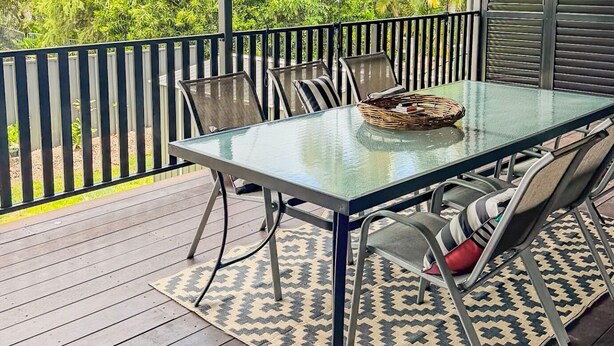 Eine überdachte Terrasse im Freien mit einem Glastisch, Metallstühlen und einem gemusterten Teppich.