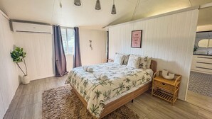 Ein Schlafzimmer mit Bett, Nachttischen, einer Pendelleuchte, einer Topfpflanze und einem Fenster mit Vorhängen.