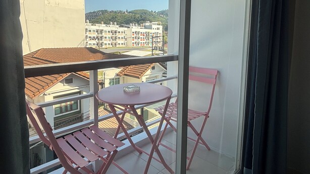 A balcony with a table and chairs, a view of buildings, and a clear sky. - Patong Gray House (Patong)