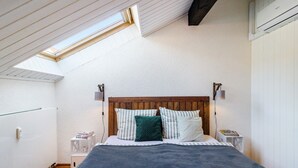 A bedroom with a sloped ceiling, a wooden headboard, a bed with striped bedding, a green pillow, and a bedside table with a lamp. - Apartment 'Stadt-Loft' with Private Terrace, Wi-Fi, and Air Conditioning (Nordhausen)