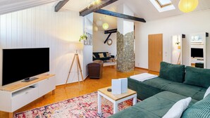 A modern living room with a flat-screen TV, a green sofa, a small table, and a large window. - Apartment 'Stadt-Loft' with Private Terrace, Wi-Fi, and Air Conditioning (Nordhausen)