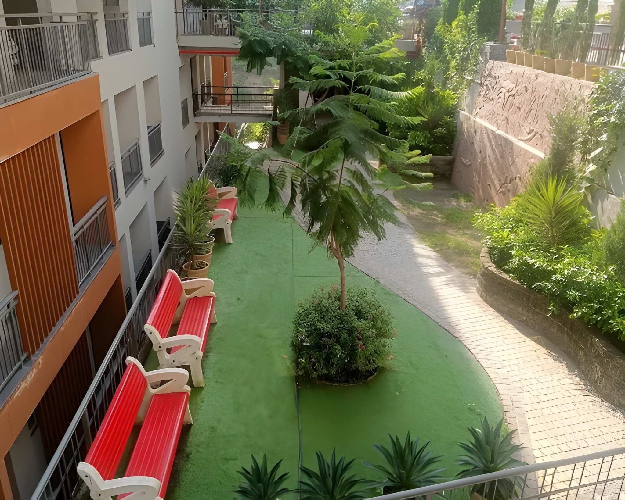 A courtyard with green artificial turf, red benches, and potted plants.