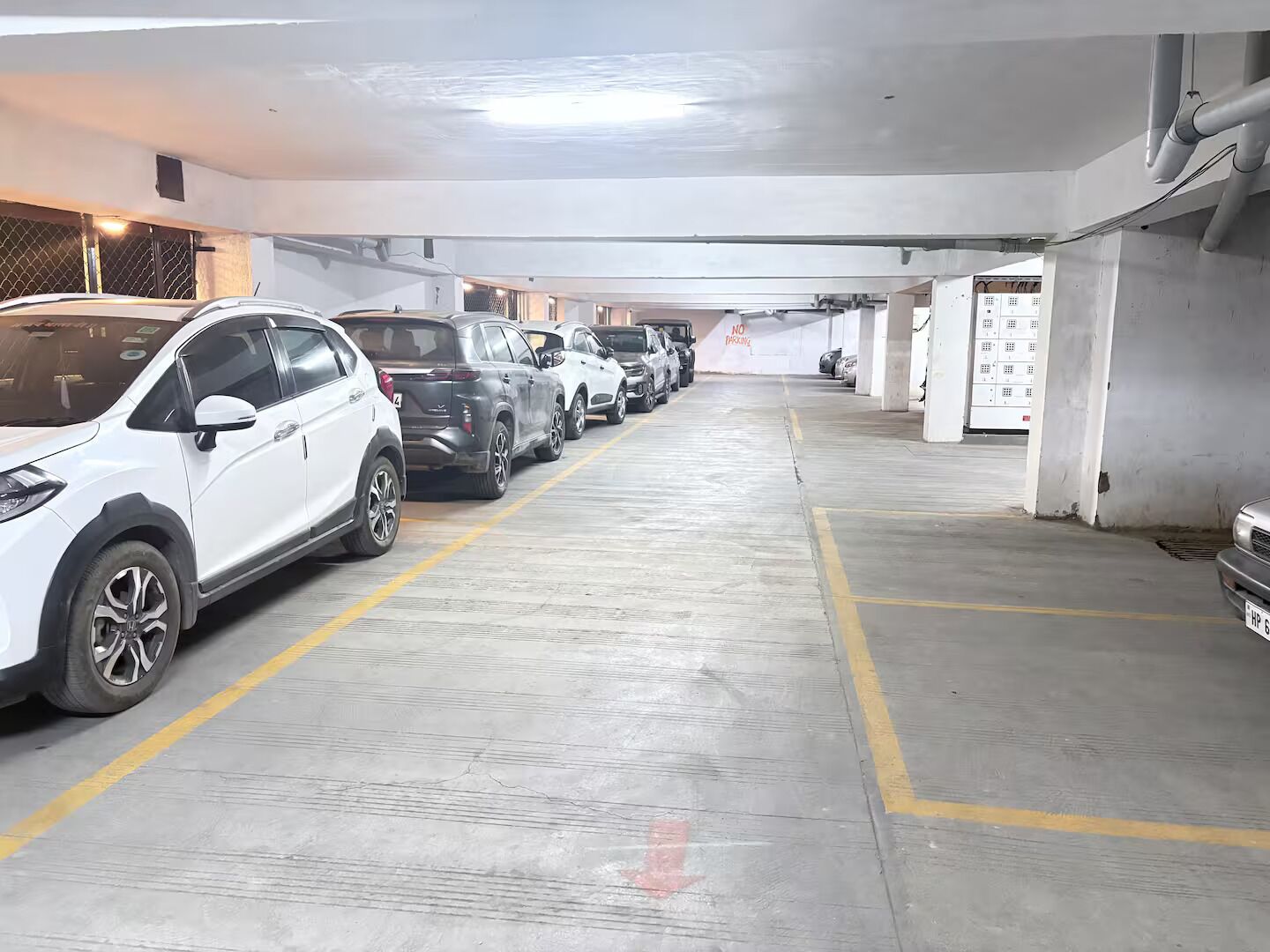 A parking garage with multiple rows of parked cars, concrete floors, and a 'No Parking' sign.