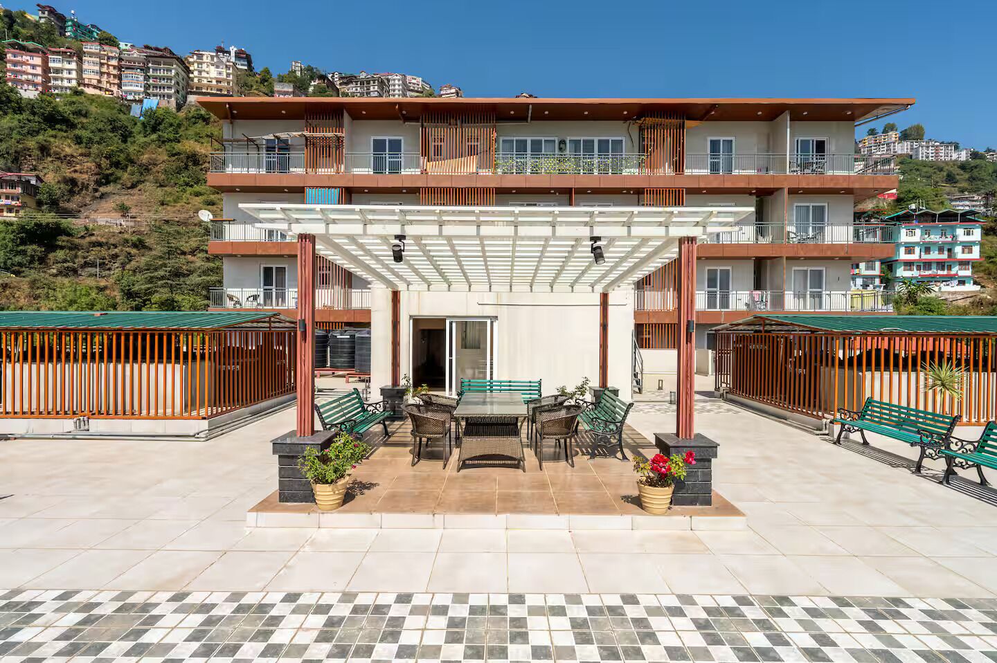 Un immeuble résidentiel à plusieurs étages doté d’un patio couvert aménagé avec des meubles d’extérieur et des plantes en pot.