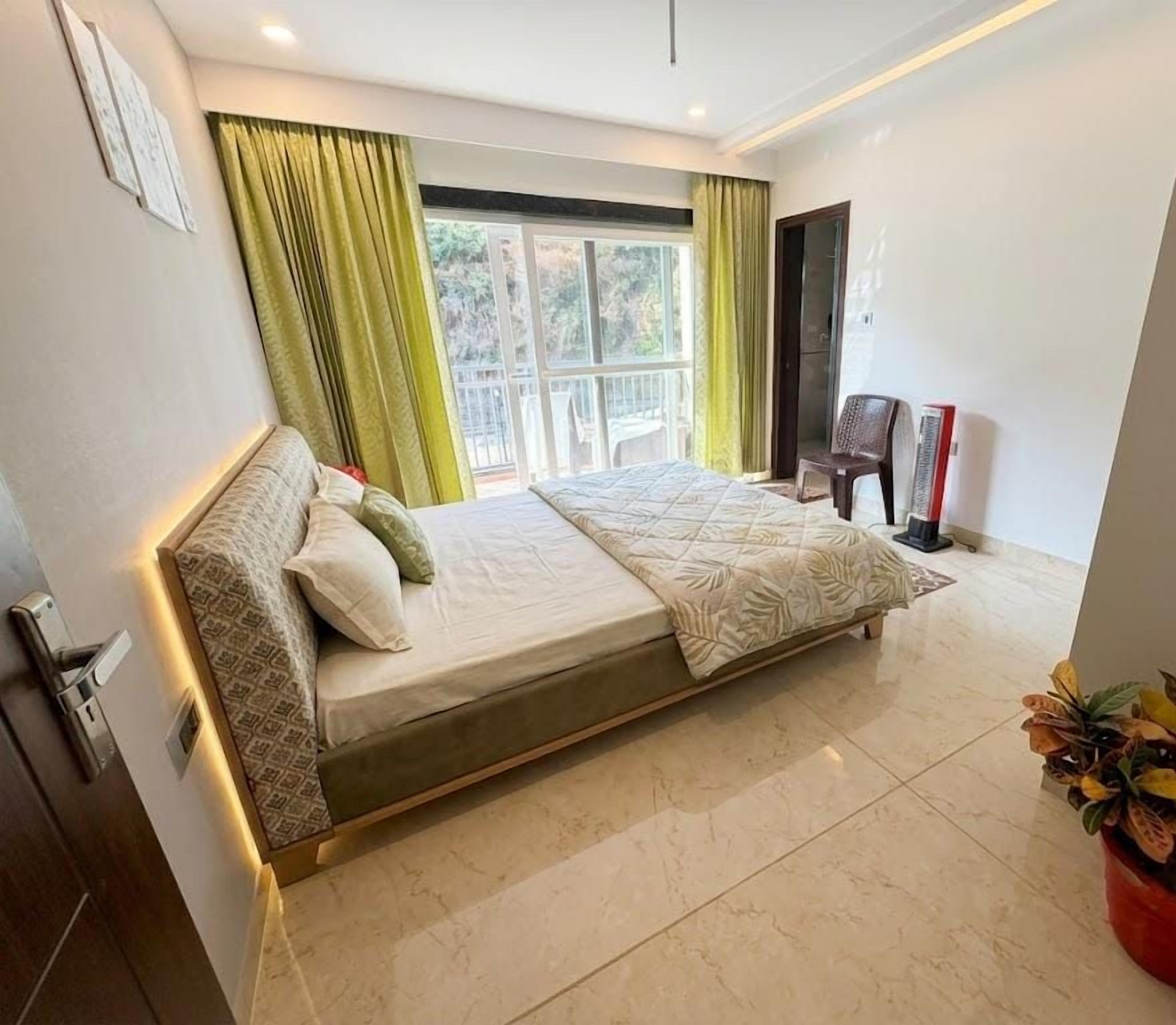 A bedroom with a bed, a window with curtains, a chair, and a potted plant.