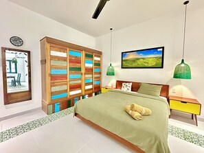 Quarto com cama, guarda-roupa de madeira, um quadro e duas luminárias pendentes verdes.
