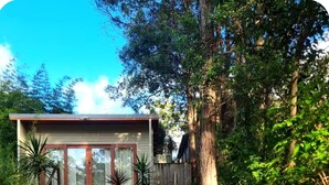 Une maison dotée d’une terrasse en bois, d’un petit patio avec des chaises et d’un chemin menant à l’entrée.