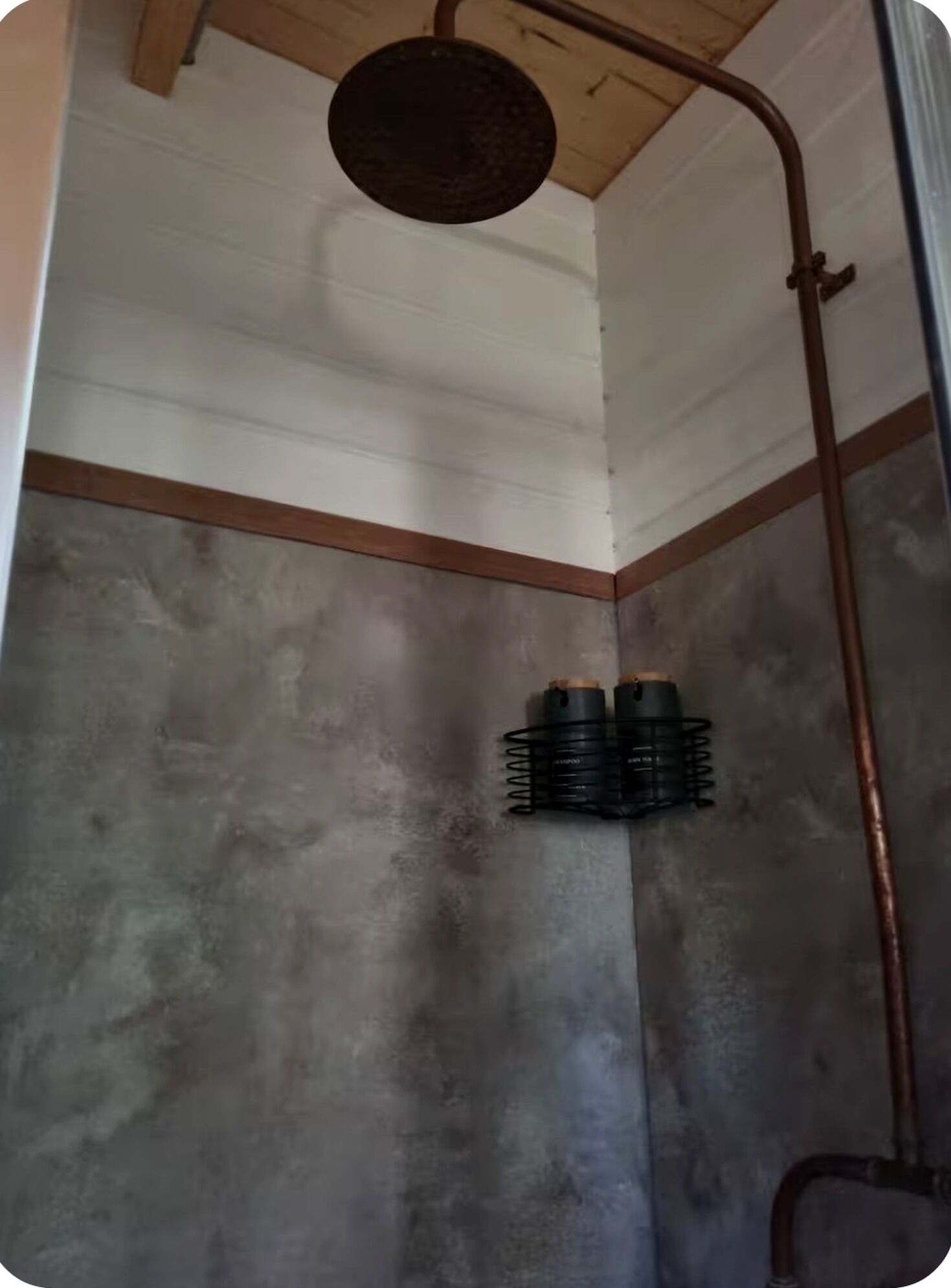 Un angolo doccia con soffitto in legno e tubatura in metallo.