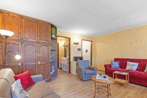 A cozy living room with a wooden cabinet, a red sofa, a blue armchair, and a small table with a tray. - Appartamento Rifugio dei Sogni (Pragelato)