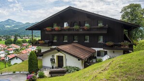 Un chalet à deux étages doté d’un balcon, d’une petite dépendance attenante et offrant une vue sur un village et des montagnes.