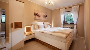 Une chambre à coucher avec un lit, des tables de chevet, un lustre, une fenêtre avec des rideaux et un tableau au mur.