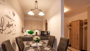 Un espace repas moderne avec une table en verre, une nappe à motifs noir et blanc et des chaises en cuir. Un mur décoratif avec du texte et une petite plante ornent l’ensemble.