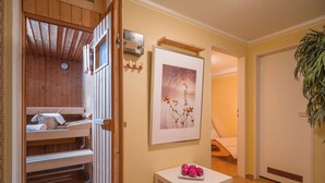 Un sauna en bois, avec des bancs et un radiateur fixé au mur, une œuvre d’art encadrée et une petite table avec des pommes.