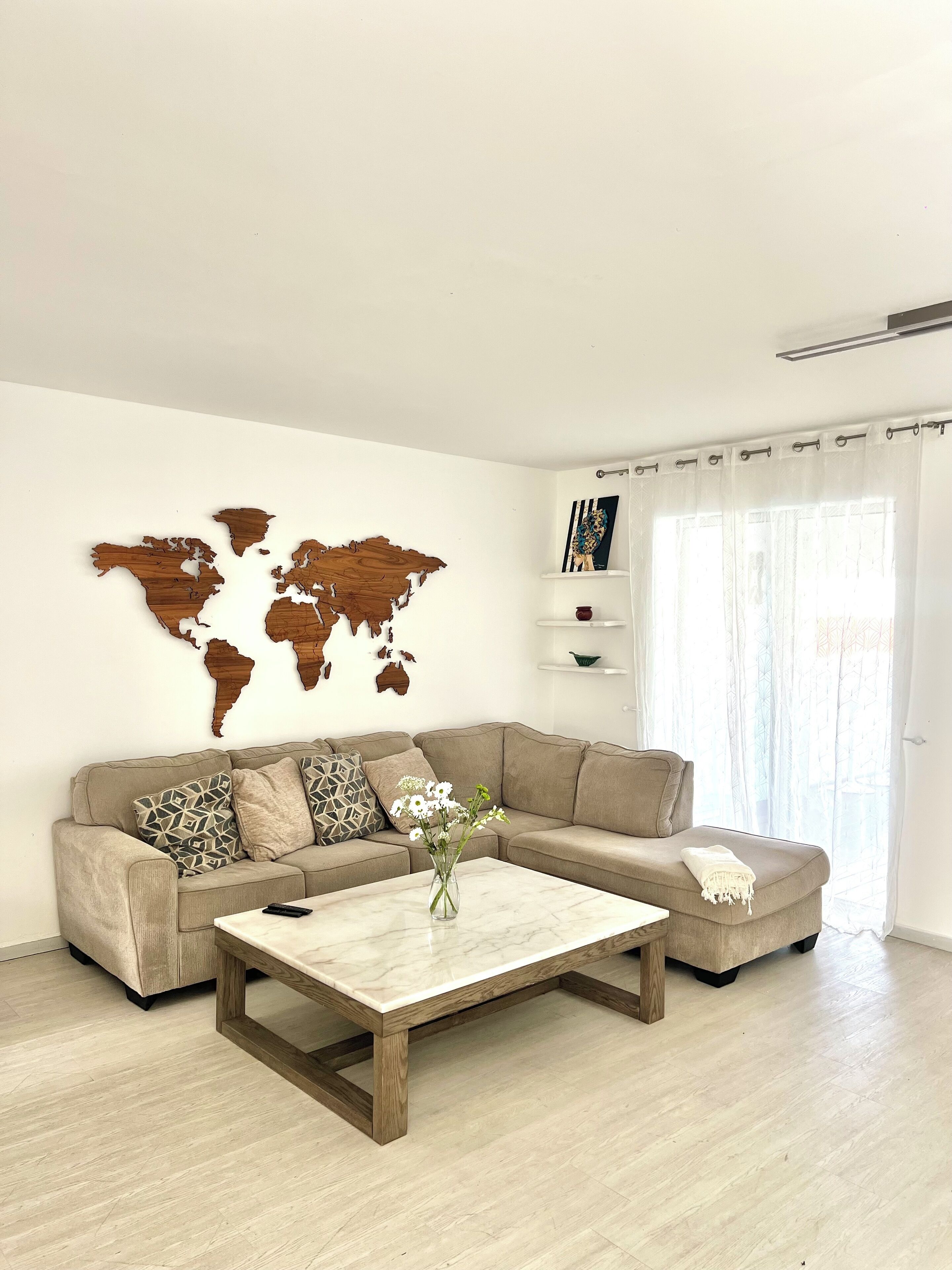 A living room with a beige sofa, a wooden coffee table, and a world map on the wall.