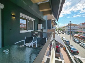 Ein Balkon mit Glastisch, weißen Stühlen und Blick auf die Straße.