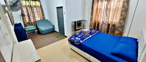 A compact room with a single bed, a chair, a small table, and a fan.