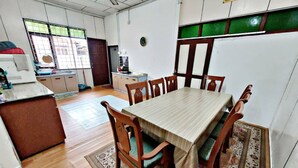 Een eethoek met een houten tafel en stoelen, een keuken op de achtergrond, en een vloerkleed met een patroon.
