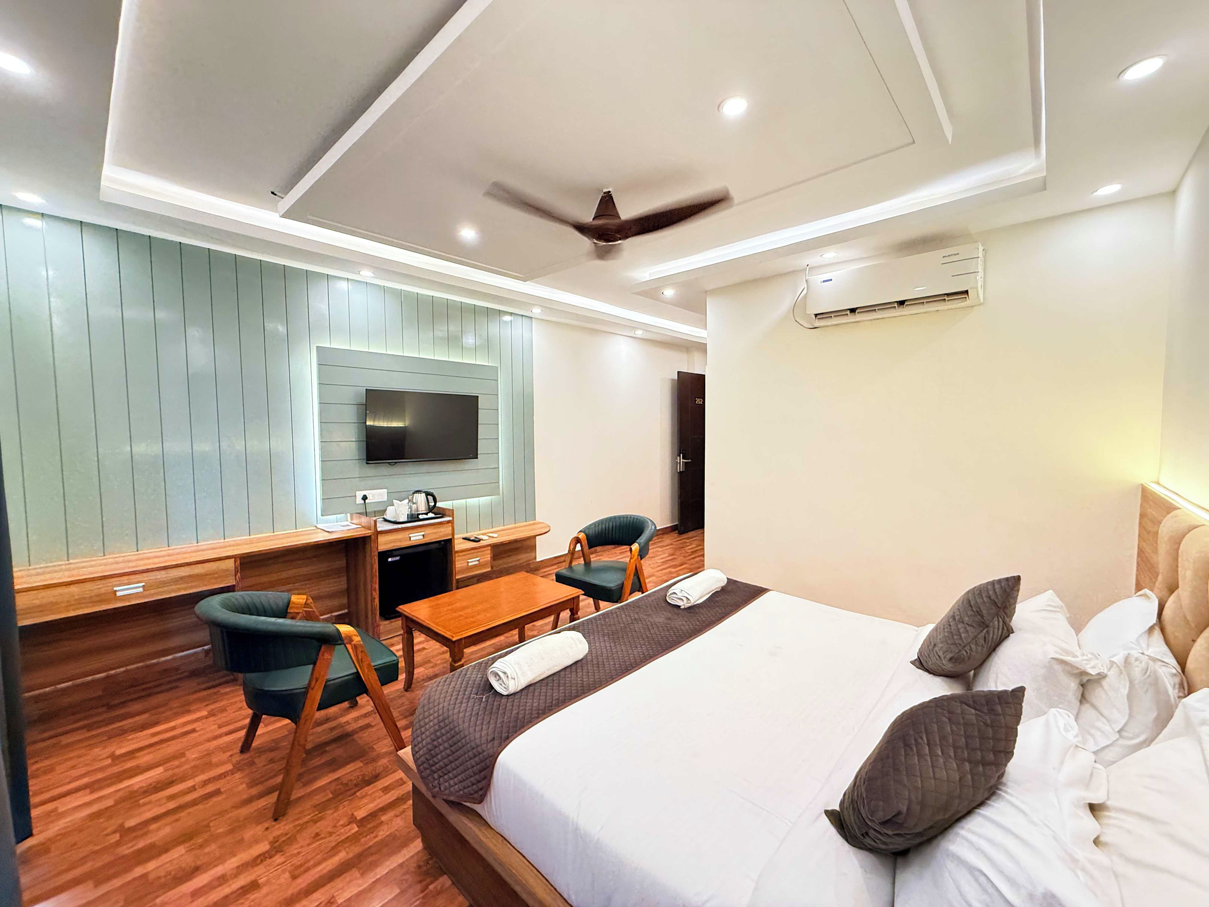 A modern hotel room with a bed, a desk, a chair, a television, and an air conditioning unit.