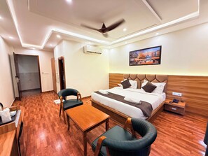 A hotel room with a bed, a desk, a chair, a table, and a ceiling fan. - The Prominence Hotel Greater Noida (Greater Noida)