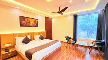 A modern hotel room with a large bed, a ceiling fan, a painting on the wall, and a window with a view of trees.
