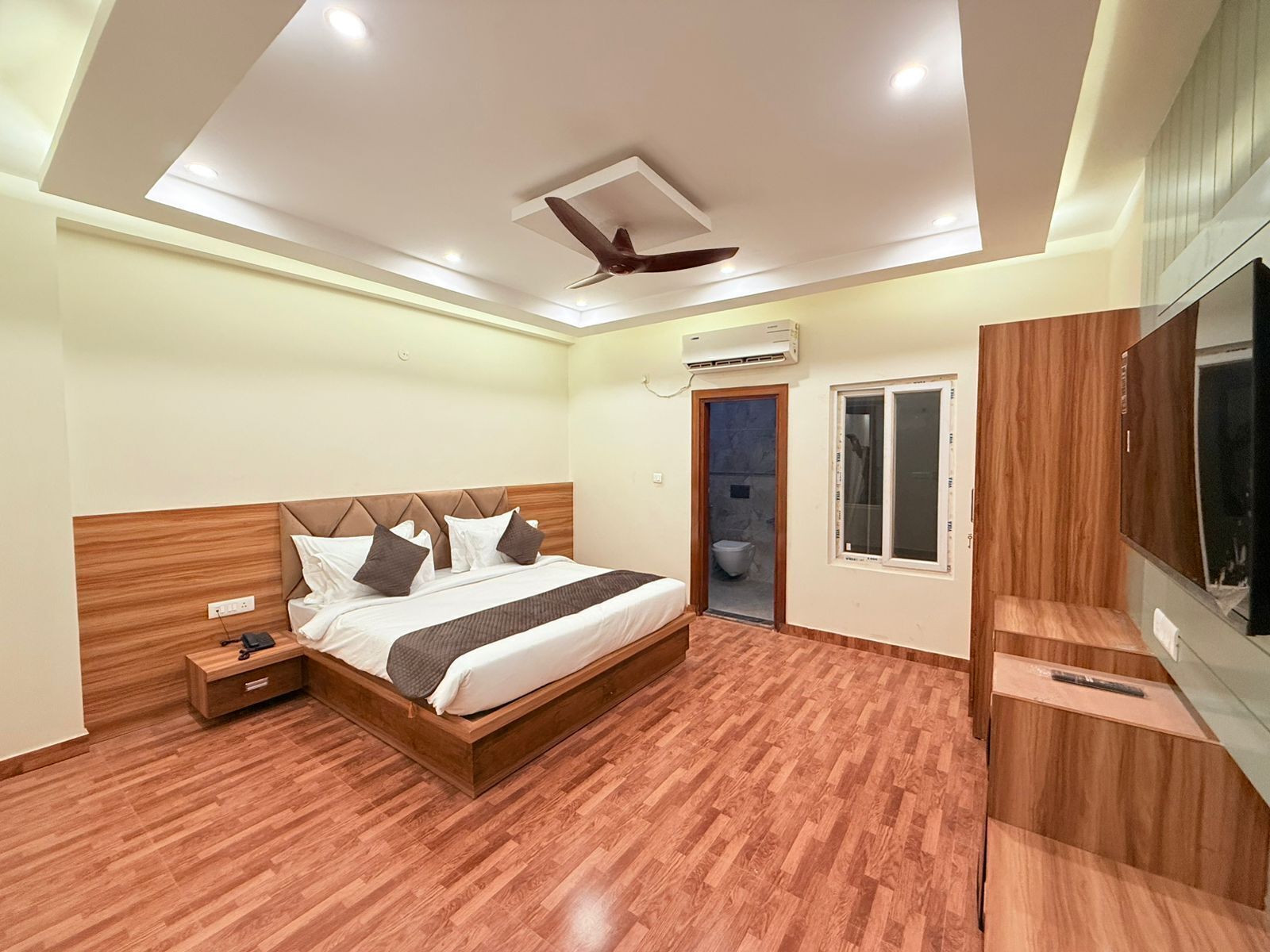 A modern bedroom with a wooden bed, a ceiling fan, a TV, and a small bedside table.