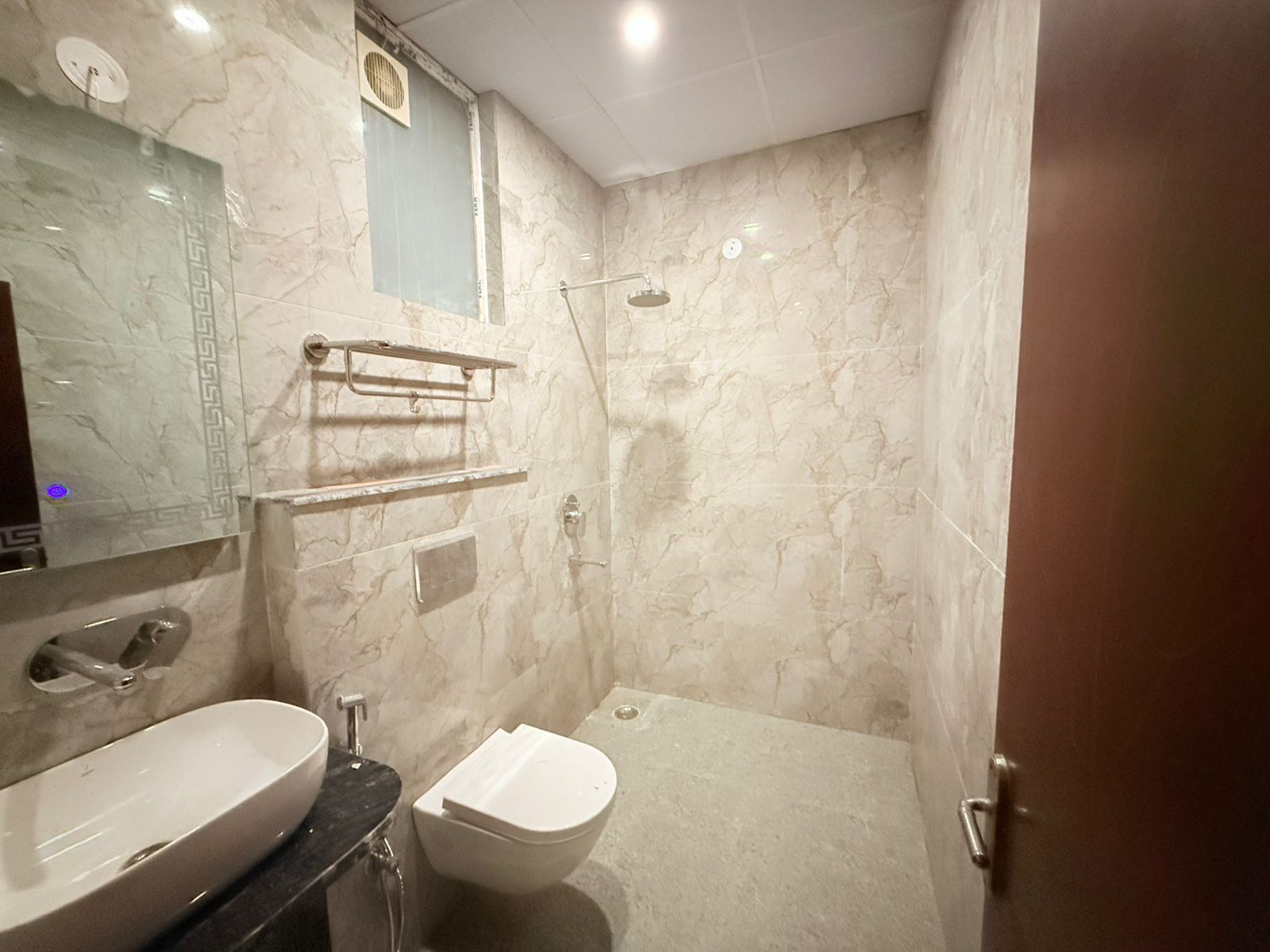 Une salle de bain avec un grand lavabo, des toilettes et une douche. On y trouve des porte-serviettes et un miroir au-dessus du lavabo.