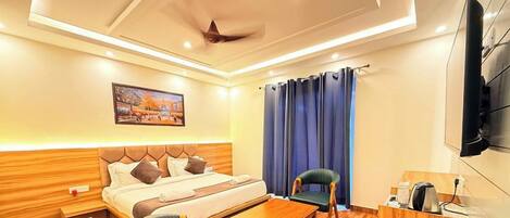 A hotel room with a bed, a desk, a chair, a television, and a ceiling fan.