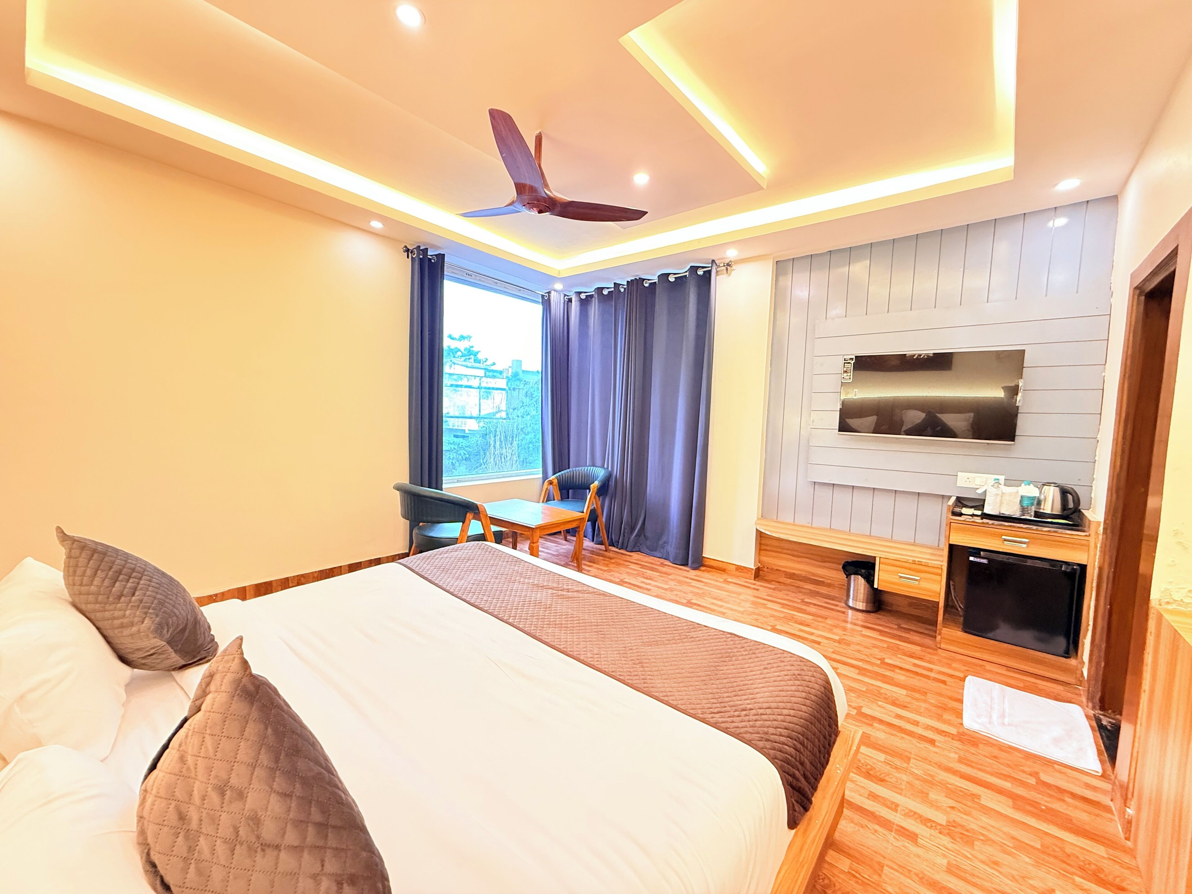 A hotel room with a bed, a desk, a chair, a ceiling fan, a TV, and a window with curtains.