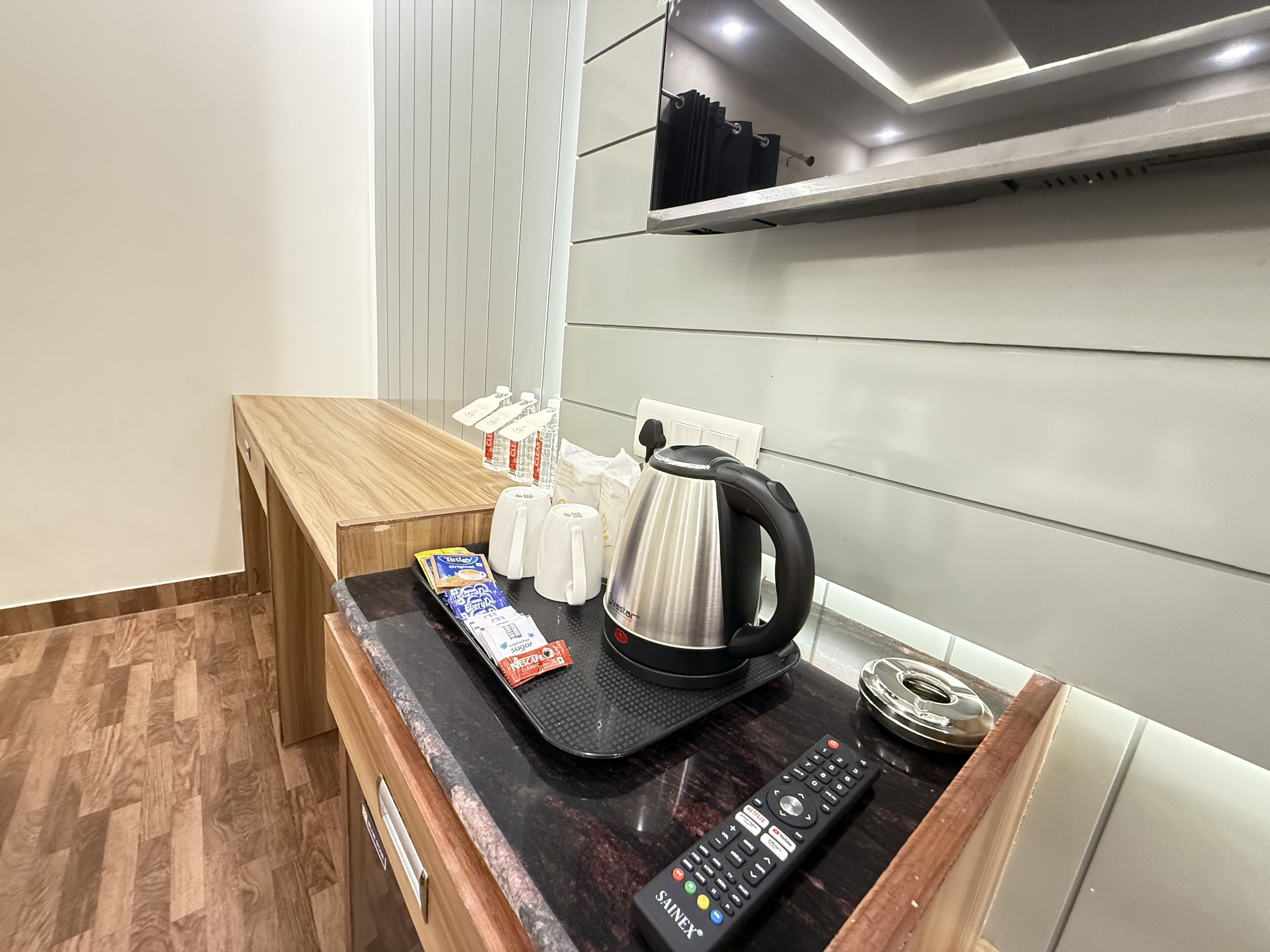 Een kitchenette met een koffiezetapparaat, een afstandsbediening en enkele verpakte etenswaren op het aanrecht.