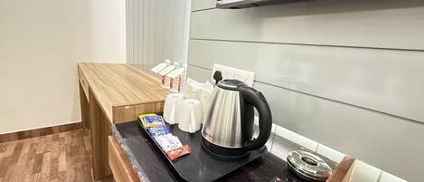 Une petite cuisine équipée d’une machine à café, d’une télécommande et de quelques aliments emballés, disposés sur le comptoir.