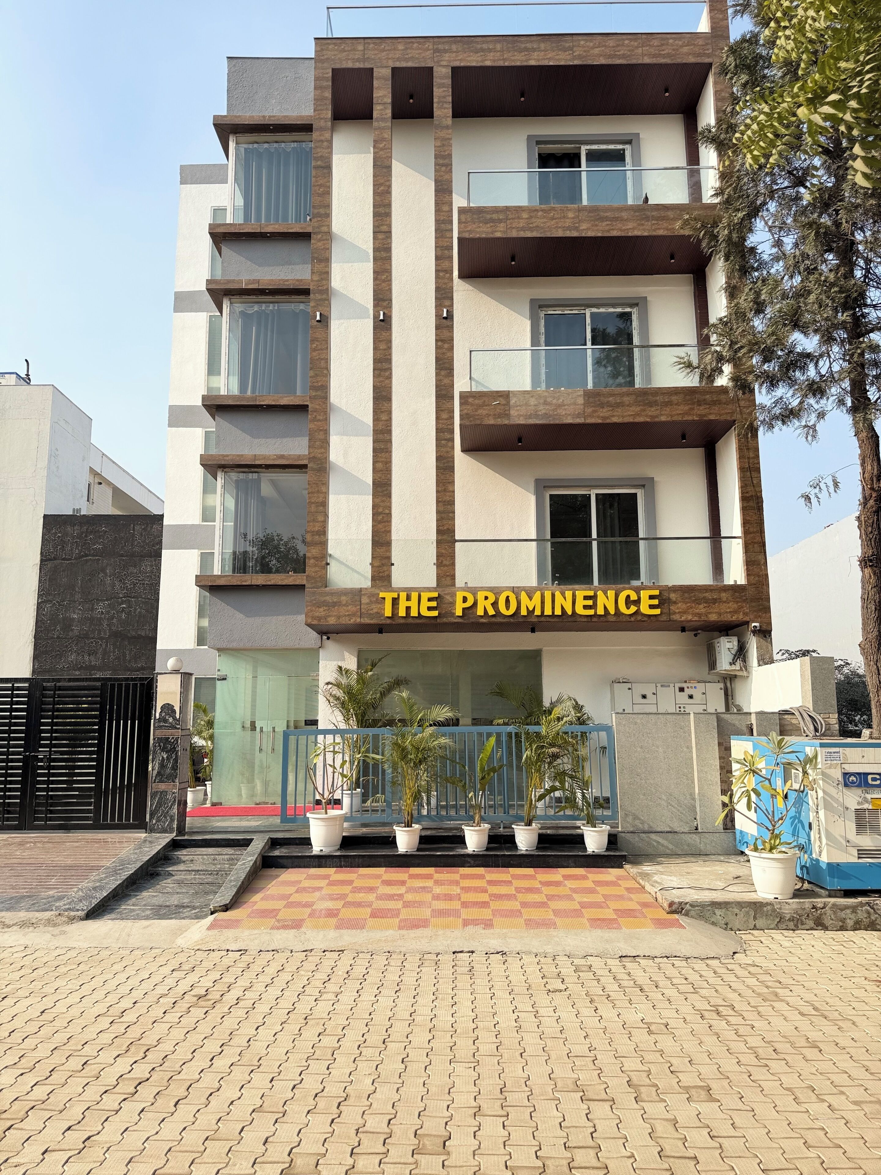 A multi-story hotel named "The Prominence" with a modern architectural design, featuring balconies and potted plants.