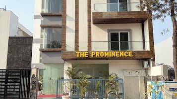A multi-story hotel named "The Prominence" with a modern architectural design, featuring balconies and potted plants.