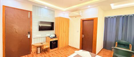 A hotel room with a bed, a desk with a TV, a ceiling fan, and a green chair.