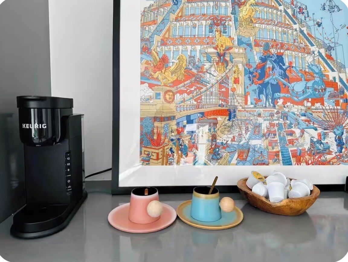 Una cafetera, dos tazas con tapa y un cuenco de tazas sobre una mesa.