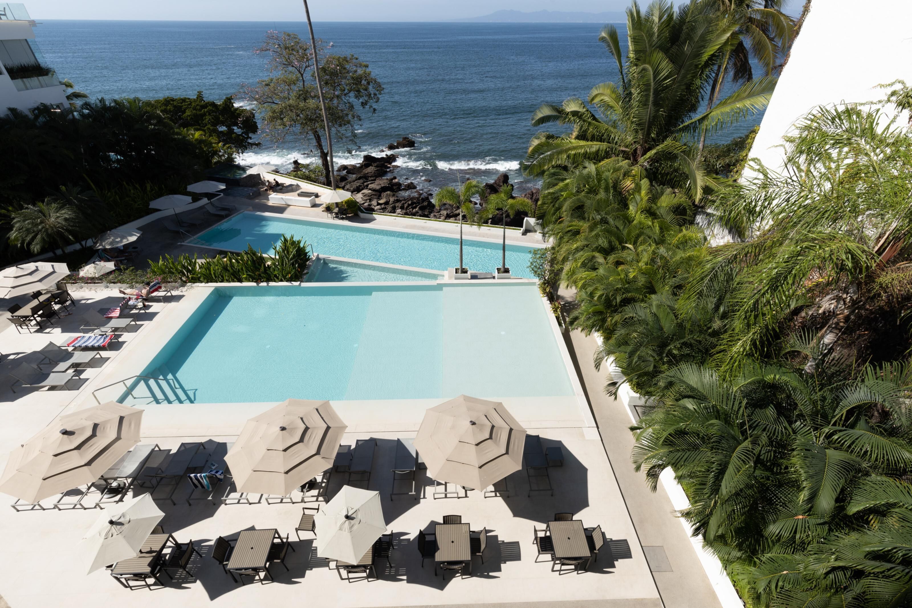 Un espace piscine sur le toit, comprenant plusieurs piscines, des chaises longues et des parasols.