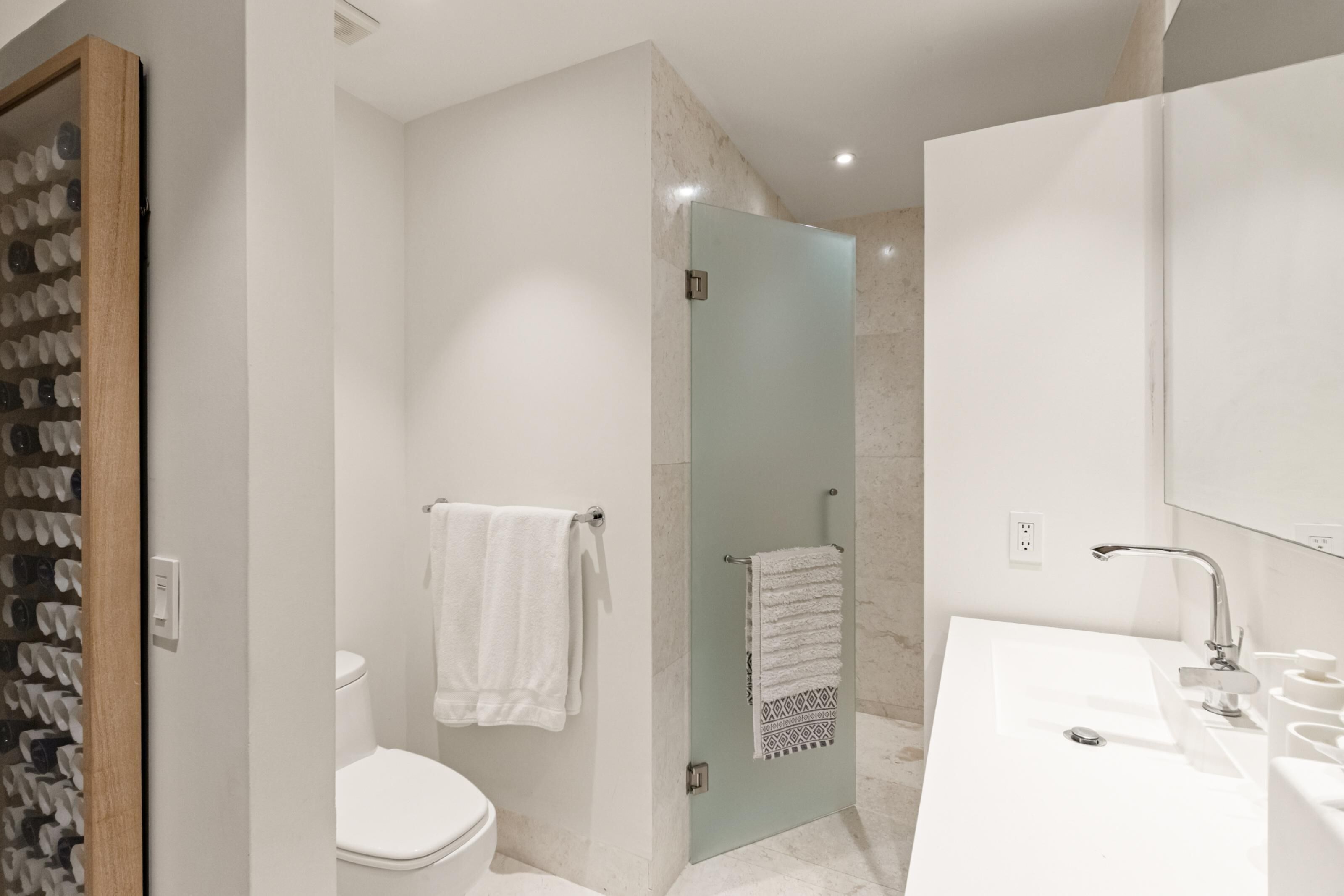 Een moderne badkamer met een douchecabine van glas, een wit toilet en een grote wastafel met spiegel.